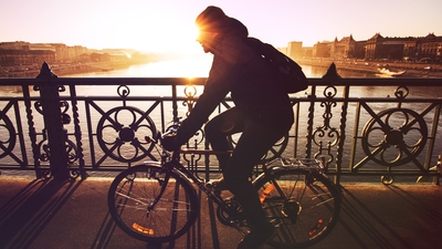 man bicycling across a city bridge in the morning