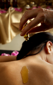 hand pouring essential oil on a woman's bare back