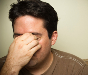 man with eyes shut, touching his forehead in stress
