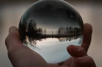hand holding reflective glass ball in front of a forest lakeshore