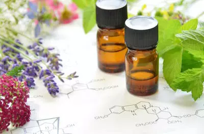 two unlabeled brown bottles of essential oils with black caps on a chemistry paper with leaves and flowers around the edges