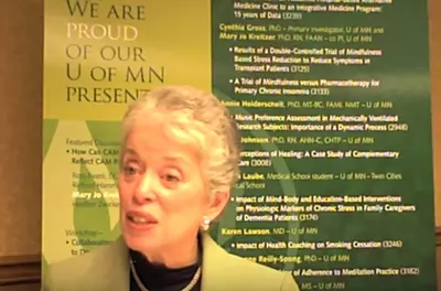 Susan Folkman speaking in front of a conference poster