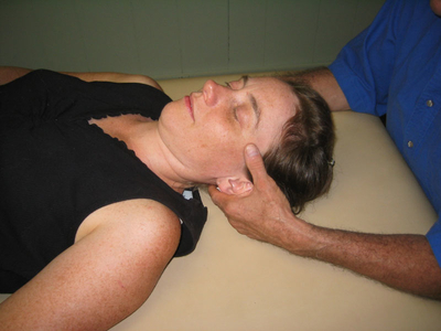 woman lying on table as man's hands touch her head