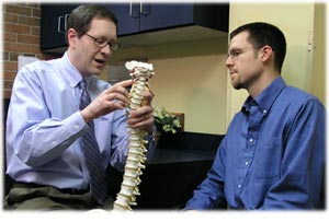 Chiroractor showing model of spine to male patient
