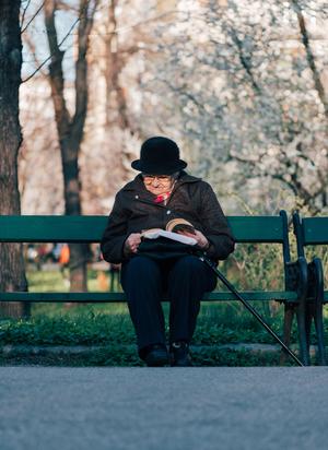 elderly person sitting on a park bench reading