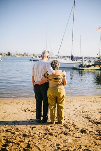 elderly man and woman facing a lake with their arms around one another