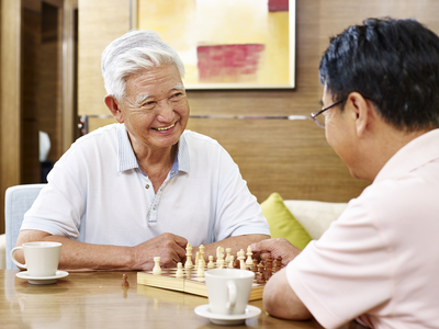 Elderly man smiles as he plays chess with a friend