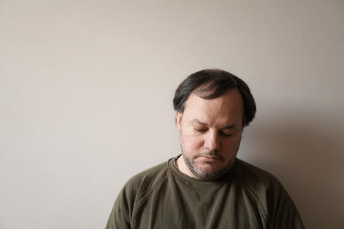 Sad man with depression and anxiety leaning against a blank wall.