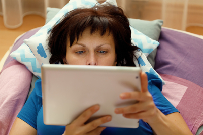 woman resting in bed and reading news on a tablet
