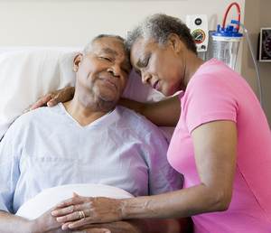 senior woman embracing a man who is lying in a hospital bed