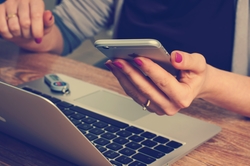 woman's hands dialing a cell phone next to her laptop