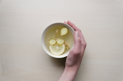 a hand wrapped around a simple mug of tea with lemon