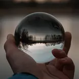 hand holding reflective glass ball in front of a forest lakeshore