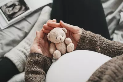 pregnant woman holding teddy bear against her stomach