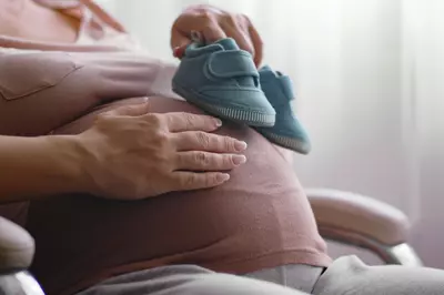 pregnant woman holding baby shoes against stomach