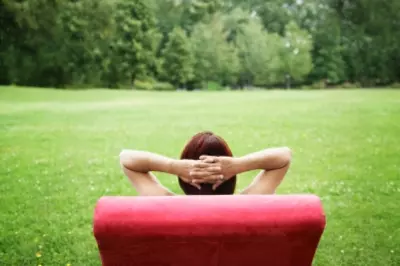 Figure sits in chair outside with hands folded behind head