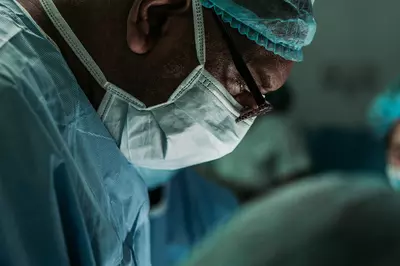 close up of a surgeon in scrubs and mask looking down at a patient
