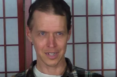 Michael smiles at the camera in front of a white and brown background.