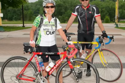Two bicyclists in biking gear and helmets smile