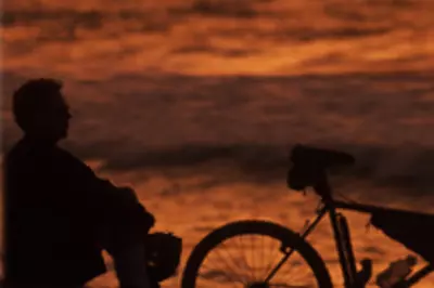 Bicyclist sits next to bike and ponders sunset on beach