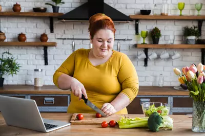 woman making salad while looking at her laptop