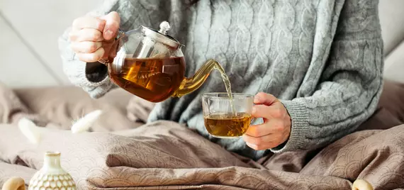 Woman in sweater pours tea into a mug while sitting in bed stock photo