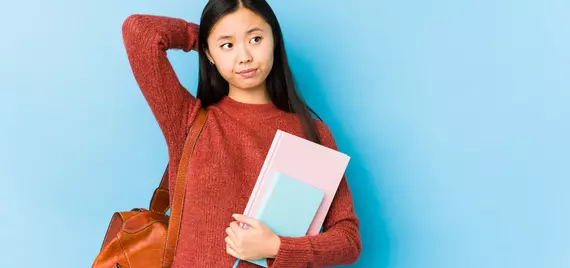 student holding books and bag looking pensive and uncertain
