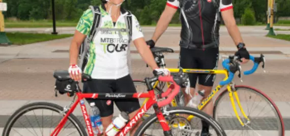 Two bicyclists in biking gear and helmets smile
