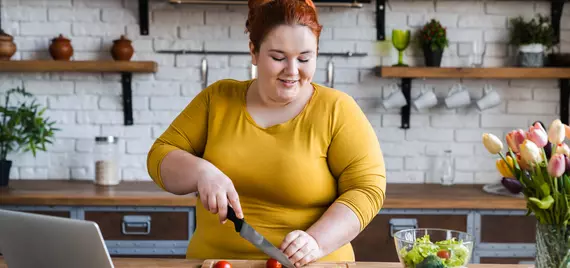 woman making salad while looking at her laptop