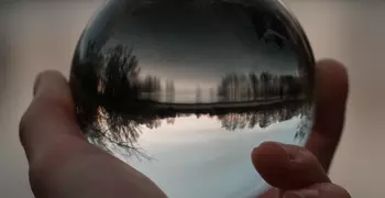hand holding reflective glass ball in front of a forest lakeshore