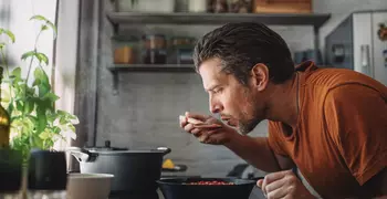 man tasting sauce from a cast iron pan