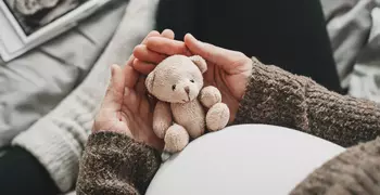 pregnant woman holding teddy bear against her stomach 