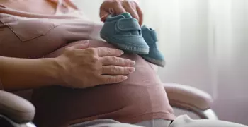 pregnant woman holding baby shoes against stomach 