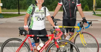 Two bicyclists in biking gear and helmets smile