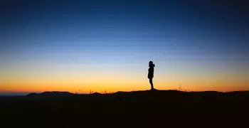 a lone silhouette standing in front of a sunset