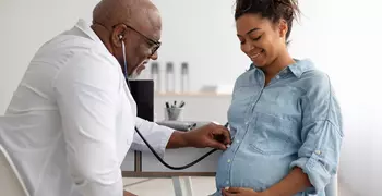 doctor listening to baby's heartbeat in pregnant woman's stomach 