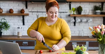 woman making salad while looking at her laptop