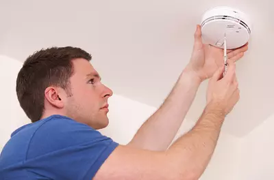 man in blue tee shirt installing a carbon monoxide detector on the ceiling
