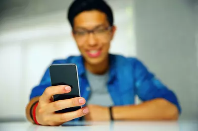 young man smiling and entering information into his phone