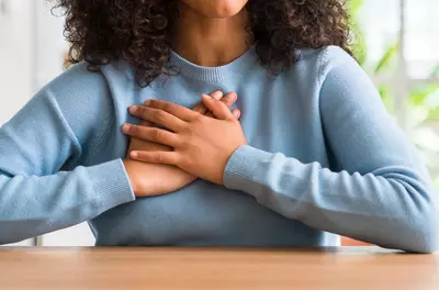 close up of person in blue sweater with hands folded over their chest