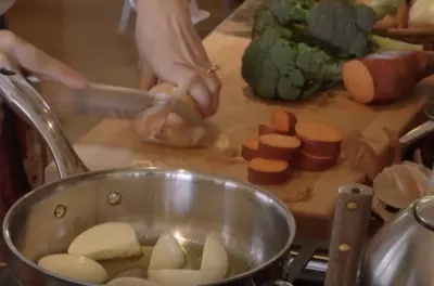 Hands chopping sweet potatoes, broccoli, and onion on a kitchen counter