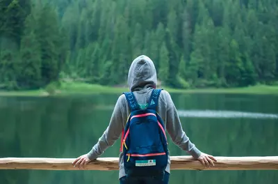 Picture of person with a backpack and hoodie from the back facing a lake and trees