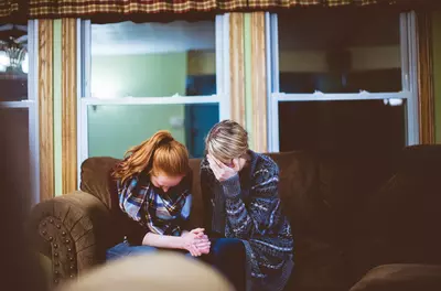 Two woman on a couch with their hands on their faces as if they are crying