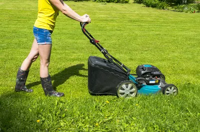 person pushing a lawn mower over green grass