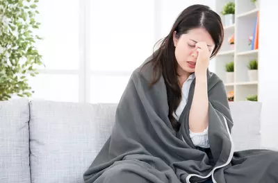 Woman sitting on a couch wrapped in a blanket looking sick