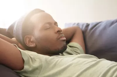 man sleeping on couch with arms behind his head
