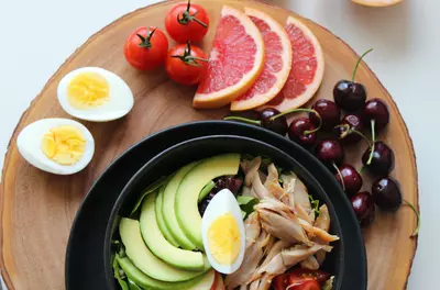 plate of colorful foods, including avocado, grapefruit, tomatoes, egg, and cherries