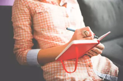 close up of hands writing in a red journal