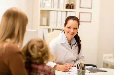 smiling white female doctor speaking with a child and adult in her office