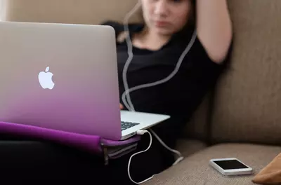 young woman on couch using laptop and wearing headphones